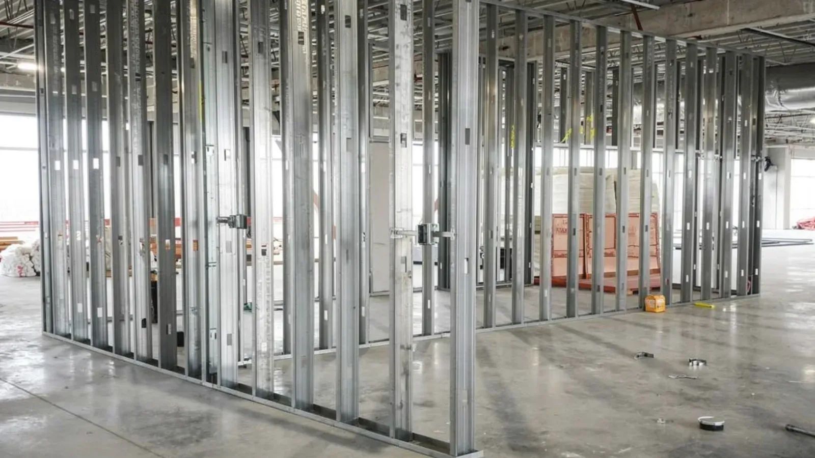 A steel stud partition wall framed on an open commercial floorplate, studs standing on bare concrete