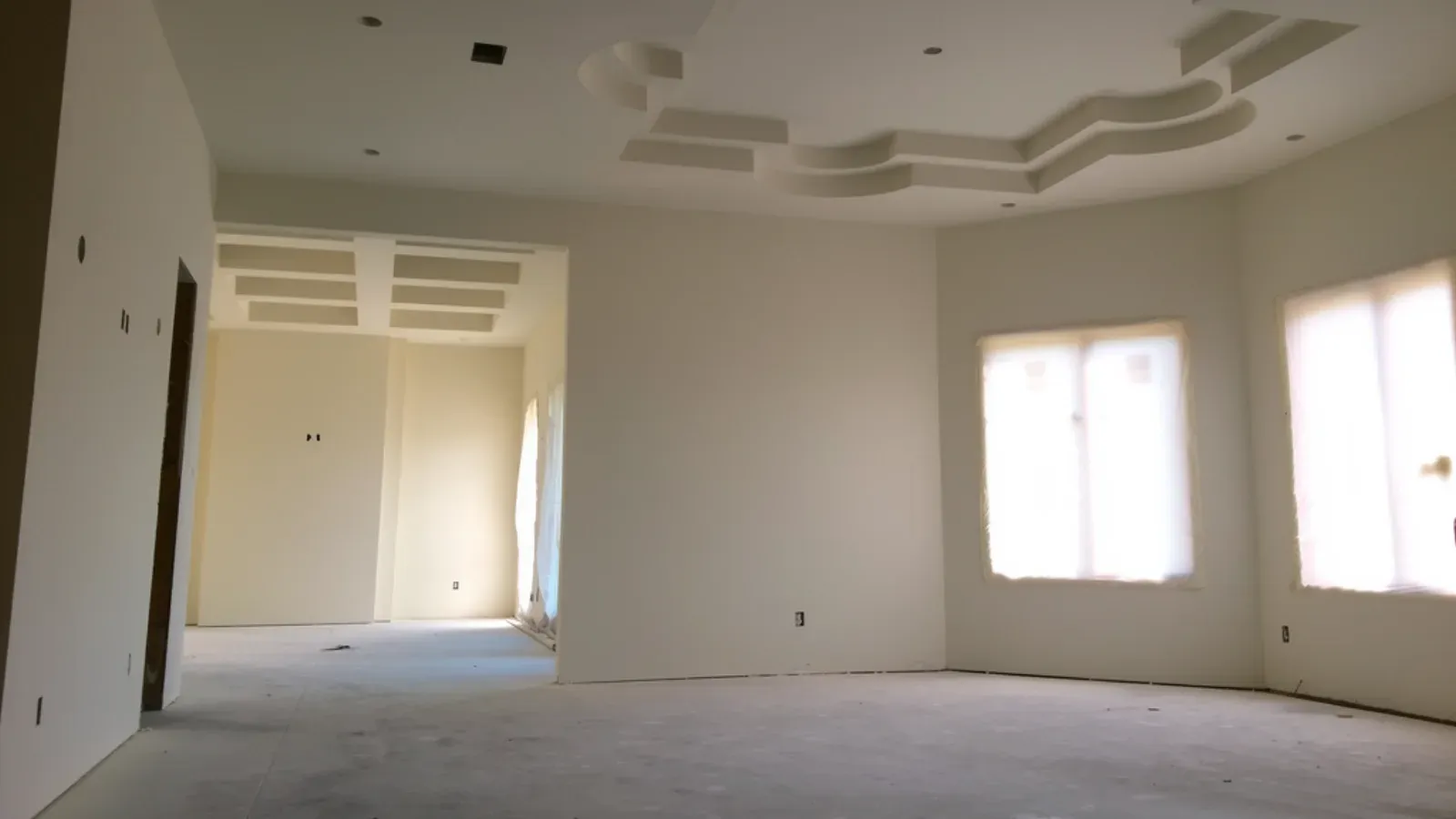 An open interior skim-coated throughout to a smooth uniform finish, with a stepped tray ceiling and plastic-masked windows