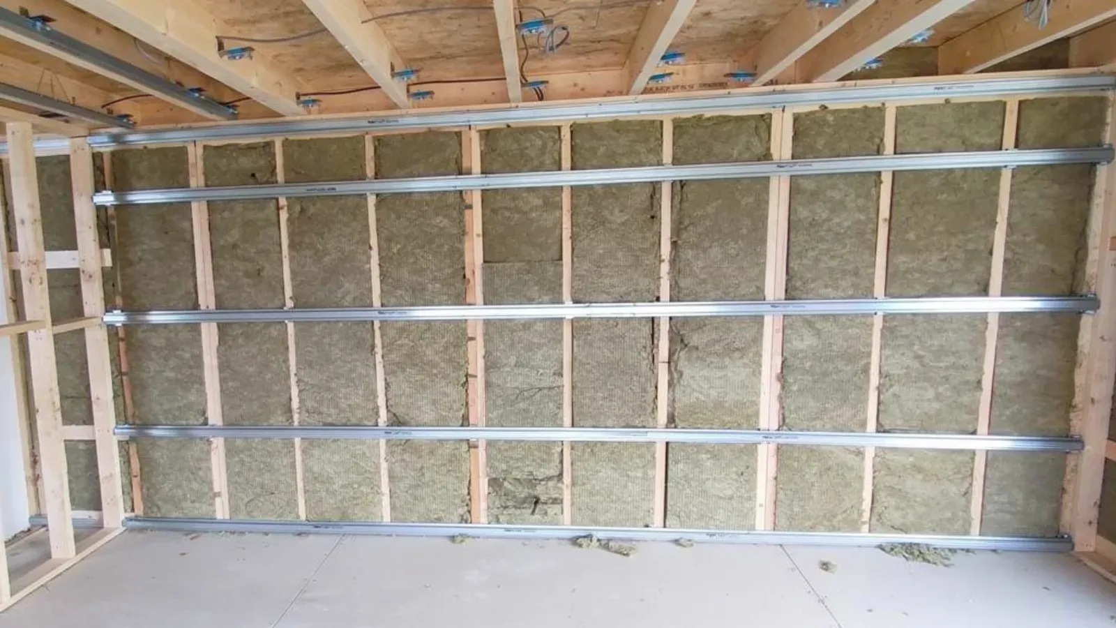 Interior stud wall with mineral wool insulation between the studs and horizontal resilient channels fixed across them, ready for a second layer of drywall